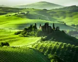 Colline verdi ondulate in Toscana, con una villa su una collina circondata da cipressi. Un sogno per un viaggio in Toscana.