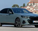 Szary BMW 520 z czarnymi felgami stoi na tle malowniczego nadmorskiego miasteczka.