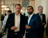 Två män i kostym håller glas med champagne. Bakom dem syns en festlig miljö med ljuskronor. Kanske en scen från "hundarna" på SVT.