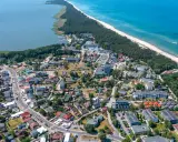 Dąbki atrakcje: widok z lotu ptaka na nadmorską miejscowość z plażą, lasem, jeziorem i zabudowaniami.