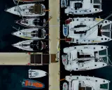 Vue aérienne d'un port avec plusieurs yachts à voile blancs amarrés, certains catamarans, et des annexes gonflables.
