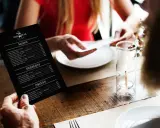 Mężczyzna trzyma czarne menu restauracji "The Dark Bear". Co to jest laminat? To trwałe menu, idealne do restauracji.