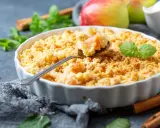 Une cuillère prélève une bouchée dorée de ce meilleur crumble aux pommes, garni de feuilles de menthe fraîche.