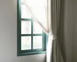 Zielone okno bez parapetu, zasłonięte jasną, zwiewną kotarą.