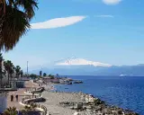 Lungomare di Reggio Calabria con vista sull'Etna innevato. Perfetto per scoprire cosa visitare a Reggio Calabria, tra palme e mare blu.