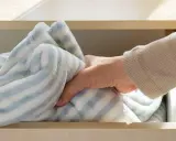 Dłoń wyjmuje z szuflady miękki, pasiasty koc. Wiesz, jak prać polar, by był jak nowy?