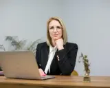 Kobieta w okularach i żakiecie siedzi przy biurku z laptopem i Statuą Temidy.