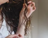 Dłoń delikatnie układa mokre, łamane loki. Włosy lśnią, tworząc naturalną fryzurę.