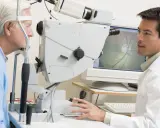 Okulista bada oko pacjenta za pomocą urządzenia. Na ekranie widoczny obraz dna oka, pomocny przy badaniu pachymetria tabela.