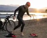Triathlet in Neoprenanzug und Badekappe, bereit für die verschiedenen triathlon distanzen. Rad und Laufschuhe liegen bereit.