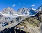 Il rifugio Marinelli, un edificio bianco e rosso, si erge su una cresta rocciosa con imponenti montagne innevate sullo sfondo.