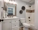 Ein kleines Bad gestalten 4qm: Weißer Waschtisch mit Marmorplatte, Spiegel mit Holzrahmen, Toilette, Duschbadewanne mit weißem Vorhang und rustikalen Akzenten.