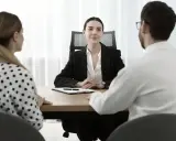 Para omawia z notariuszem podział majątku. Kobieta w kropki i mężczyzna w białej koszuli siedzą naprzeciwko urzędniczki.