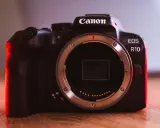 Canon EOS R10 w teście. Ciemna obudowa aparatu z czerwonym podświetleniem, widoczny bagnet obiektywu.