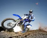 Motocyklista na Yamasze w skoku, unosząc się nad ziemią. W tle błękitne niebo, a z pod kół wzbija się kurz. Ciekawe, ile jedzie cross 125 w takim momencie!