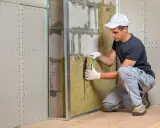 Un ouvrier installe un isolant dans une ossature métallique, étape clé pour une isolation thermique et acoustique performante.