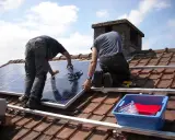 Deux ouvriers installent des panneaux solaires sur un toit. Une demande de travaux panneau solaire est en cours.