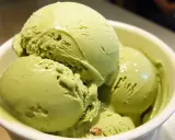 Un tazón blanco lleno de cremoso helado de pistacho, con trozos visibles de pistacho en algunas bolas.