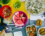 Bunte Schüssel mit Wassermelone, Kartoffelsalat, Trauben und Tomatensalat – leckere Picknick-Snacks für einen sonnigen Tag.