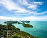 Grüne Inseln ragen aus türkisfarbenem Wasser im Nationalpark Thailand. Kleine Boote gleiten über die ruhige See unter einem blauen Himmel mit weißen Wolken.