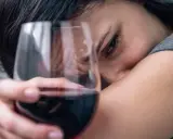 Smutna twarz kobiety z kieliszkiem wina. Czy to jeden z 6 objawów uzależnienia od alkoholu?