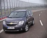 Szary Chevrolet Orlando 1.8 benzyna na pustej drodze, za barierami dźwiękochłonnymi.