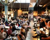 Folk äter och umgås på en livlig **Ringen food court**. Många bord är upptagna, stämningen är social och maten ser god ut.