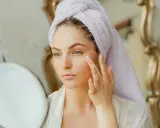 Kobieta z ręcznikiem na głowie aplikuje krem na twarz, przygotowując się do swojego codziennego glow up.