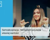 Uśmiechnięta kobieta w koronie, pewna siebie, pokazuje gestem, że jest osobą wartościową.