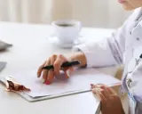 Médica revisa historial para tratamiento de hiperplasia endometrial. En su escritorio, laptop, tablet y café.