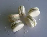 Cinq macarons vanille, délicatement posés sur une surface grise parsemée de miettes.