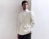 A Black tie wedding guest man in a cream double-breasted tuxedo with a matching bow tie, looking dapper.