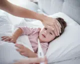 Mama sprawdza temperaturę chorego dziecka, martwiąc się przegrzaniem.