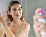 Frau sprüht sich Trockenshampoo ins Haar, um es aufzufrischen. So einfach ist es, wie man Trockenshampoo benutzt.