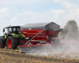 Traktor z rozsiewaczem wapna RCW 1300 marki UNIA na polu. To idealne rozwiązanie, jakie wapno pod warzywa, by zapewnić im najlepsze warunki do wzrostu.