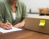 Kto płaci za przesyłkę w przypadku reklamacji? Kobieta wypełnia dokumenty przy kartonie z napisem "RETURN".