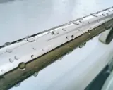 Krople deszczu na rurce ze **stali szczotkowanej**, odbijające światło.