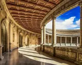 Ein sonnenbeschienener Arkadengang mit kunstvoller Holzdecke und Säulen, der zum Innenhof der Alhambra Moschee führt.