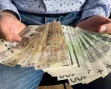 Ręce trzymające stos banknotów 100 zł i 200 zł. To darowizna od rodziców na nowy cel.