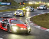Un Audi R8 rojo y negro compite en las 24 Horas Nürburgring, con otros coches de carreras en la pista mojada.