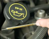 Sprawdzanie poziomu oleju silnikowego. Na bagnecie widoczne oznaczenia "ADD" i "SAFE", a na korku symbol i oznaczenie 5W-20.