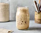 Aktiver Sauerteig im Glas, bereit für das Ansetzen mit dem Thermomix. Daneben ein Glas mit Mehl und ein Behälter mit Küchenutensilien.