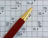 Ein roter Stift liegt auf einem Kreuzworträtsel mit deutschen Begriffen.