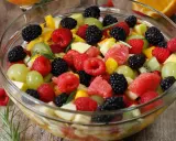 Un bol de salade de fruits frais et colorée, garnie de framboises, mûres, raisins verts, morceaux de pomme, pamplemousse et kiwi.