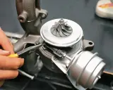 Dłoń z kombinerkami reguluje mechanizm turbosprężarki, precyzyjnie ustawiając geometrię turbiny.