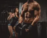 Mann mit Hanteln, Frau mit Langhantel im Hintergrund. Fokus auf Muskelaufbau durch **Hypertrophie Training**.