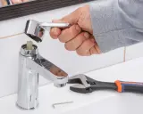 Mano desmontando grifo monomando sin tornillo. Llave inglesa y llave Allen a un lado.