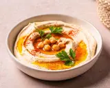 Cremiger Hummus in einer Schüssel, garniert mit Kichererbsen, Petersilie und Paprikapulver. Ein köstliches Gericht mit Hummus, bereit zum Genießen.