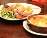 Un plat de spécialité auvergnate : pommes de terre, jambon cru, salade et un gratin de fromage fondant.