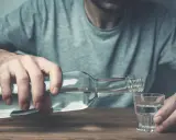 Mężczyzna nalewa alkohol do kieliszka. Czy wszywka jest skuteczna w walce z nałogiem?